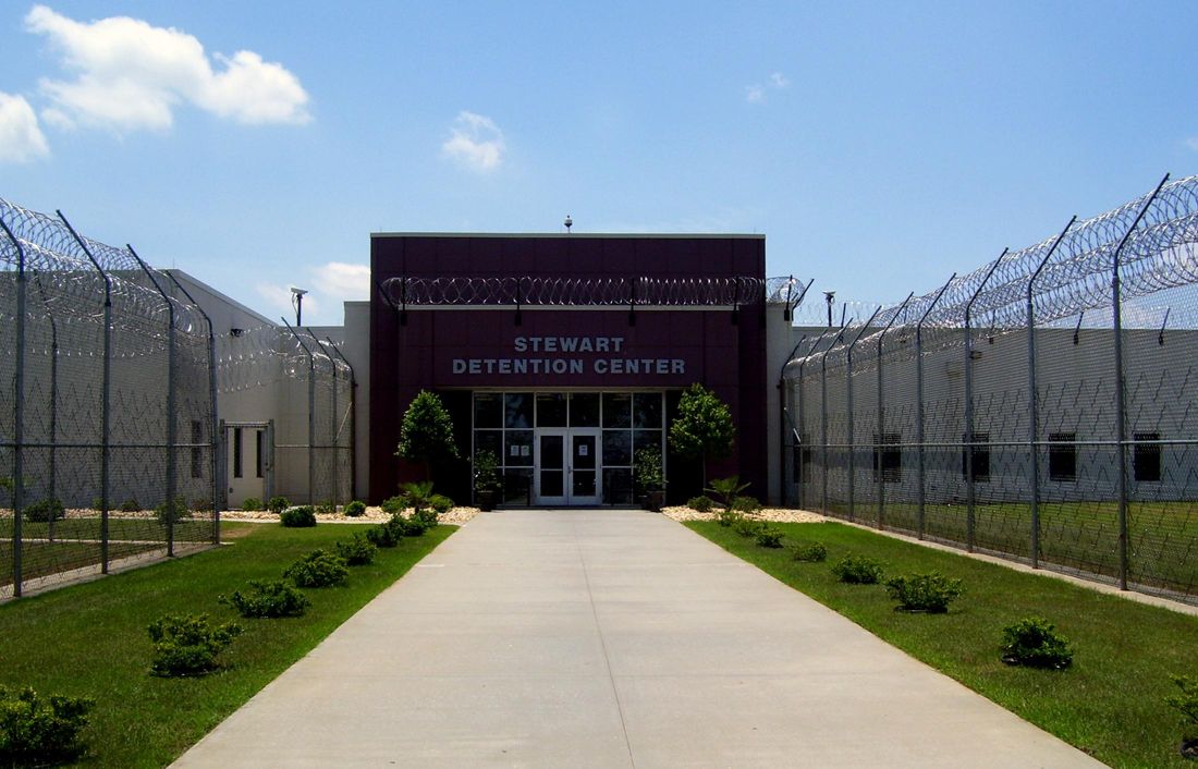 The entrance to Stewart Detention Center, with a concrete walkway between fences topped with razor wire.