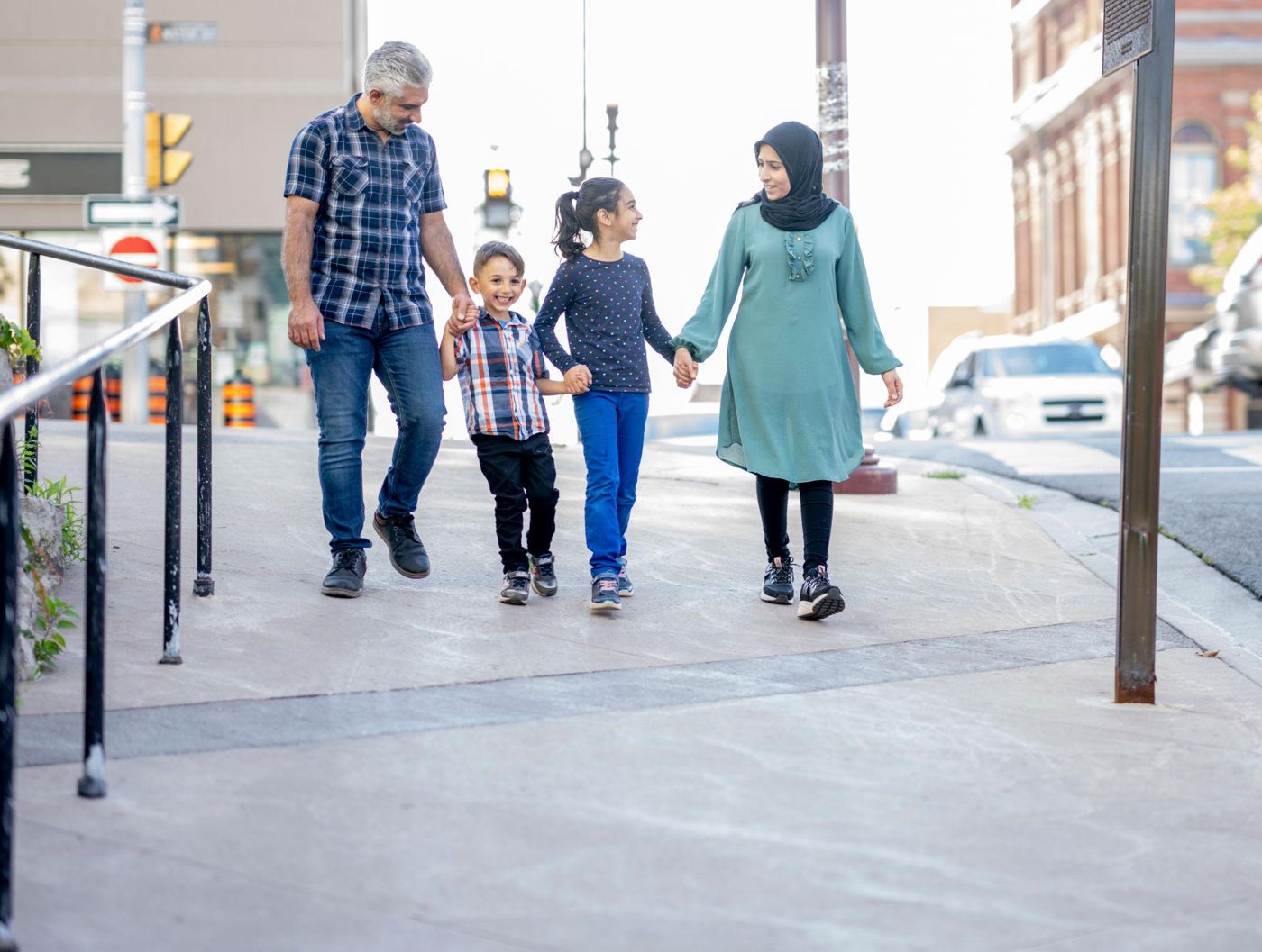 A mother, father, daughter and son walking together down a city street, holding hands and smiling.
